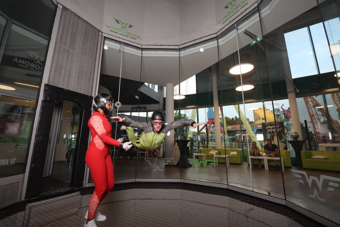 Zwei Personen in einem Windkanal, eine steht, eine fliegt.